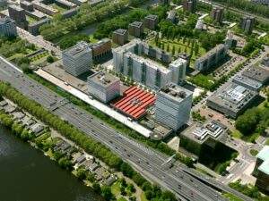 Luchtfoto van het Koningin Wilhelminaplein in Amsterdam met kantoren, woongebouwen en de snelweg A10 op de voorgrond.